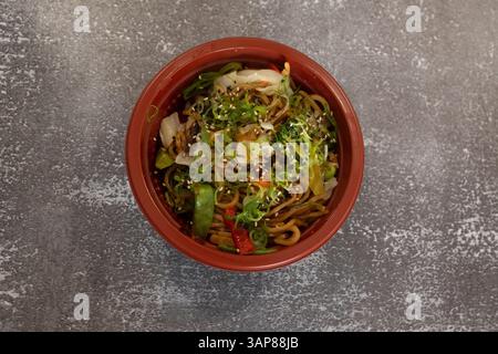 Spaghetti caldi yakisoba al vapore con verdure colorate, semi di sesamo e una salsa salata, serviti in un recipiente rosso Foto Stock