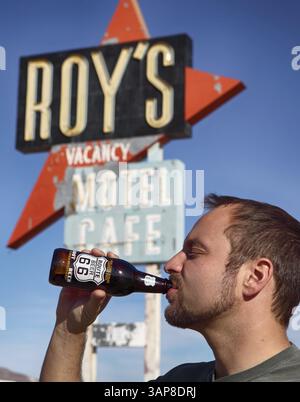 Uomo che beve una birra alla radice di fronte al cartello del Roy's Motel sulla Route 66 in California, Stati Uniti, Nord America Foto Stock