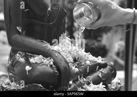 Innaffiare a mano acqua con ghirlande e gelsomino in una ciotola d'argento sulla statua nera del Buddha nel giorno di Capodanno della tradizione tailandese di Songkarn Foto Stock