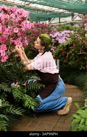 Una giovane donna nutre fiori in fiore in una serra, mostrando la sua passione per il giardinaggio. Foto Stock