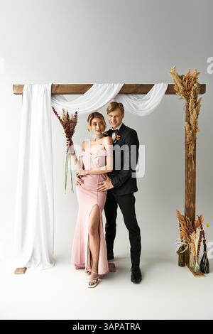 Una giovane coppia si erge insieme sotto un bellissimo arco, celebrando il loro matrimonio di primavera con stile. Foto Stock