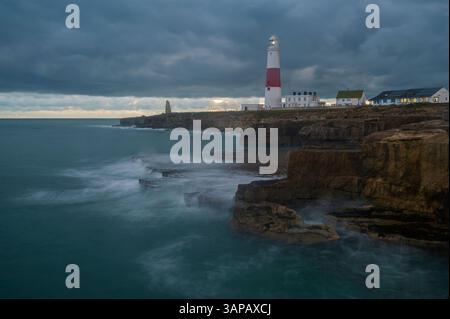 Faro di Portland Bill, Dorset, Inghilterra, con onde che si infrangono sulle sporgenze di pietra di Portland in primo piano e un cielo mooso alle spalle Foto Stock