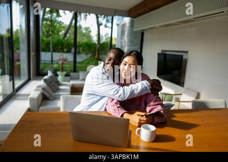 Felice coppia multietnica che utilizza un notebook, acquista online con le vendite, gioca insieme Foto Stock