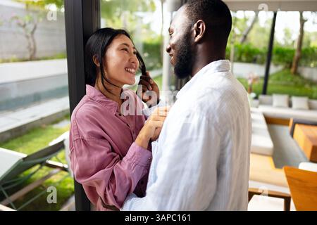 Giovani coppie diverse che sorridono gioiosamente insieme nel loro luminoso soggiorno, indossando abiti casual Foto Stock