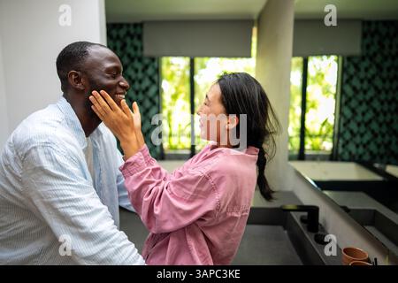 Giovani coppie diverse che sorridono gioiosamente insieme nel loro luminoso soggiorno, indossando abiti casual Foto Stock