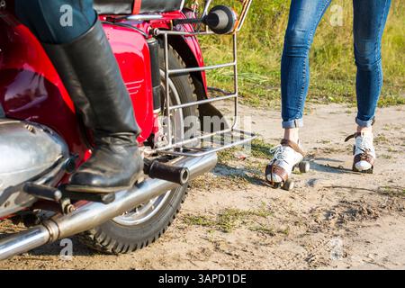 Un uomo e una donna sono in piedi accanto a una motocicletta rossa. Quell'uomo indossa una camicia bianca e un cappello. La donna indossa una camicia a quadri e jeans blu Foto Stock