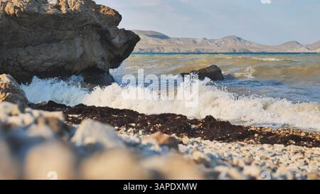 Onde che si infrangono sulla spiaggia rocciosa di Crimea con montagne sullo sfondo Foto Stock