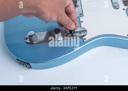 Uno scatto ravvicinato di una mano che regola l'interruttore di selezione su una chitarra elettrica blu, perfetto per la musica, gli strumenti e i progetti relativi alla chitarra. Foto Stock