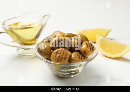 Deliziose olive verdi grigliate, olio e fette di limone sul tavolo bianco, primo piano Foto Stock