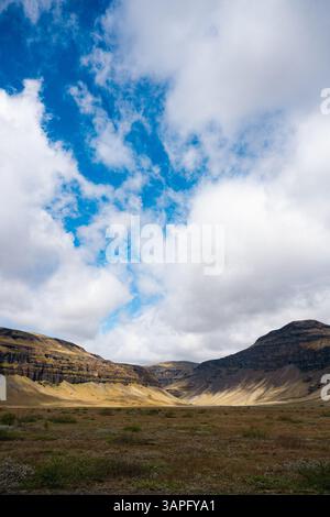 Suggestivo paesaggio della valle islandese sotto un cielo dinamico, con colline dorate e scogliere aspre illuminate dalla luce del sole che si infrangono tra le nuvole. Foto Stock