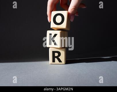 Obiettivi OKR e simbolo dei risultati chiave. Cubi in legno con parole obiettivi OKR e risultati chiave. Mano d'affari. Splendido sfondo grigio. Affari A. Foto Stock