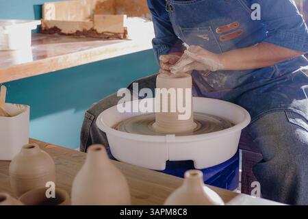 Primo piano delle mani di una donna latina che plasmano un pezzo di ceramica nel suo laboratorio. L'immagine cattura lo sforzo, la messa a fuoco e i dettagli realizzati a mano. Foto Stock
