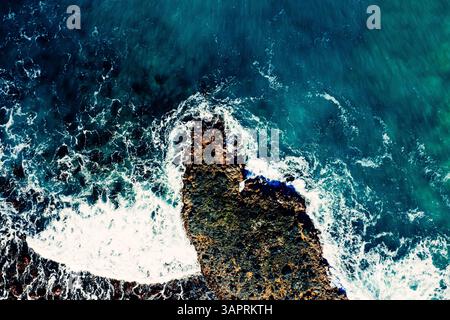 Vista dall'alto del drone sulle onde schiumose che colpiscono le rocce lungo la costa Foto Stock