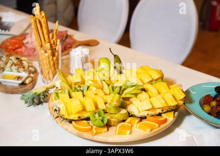 Vivace assortimento di frutta tropicale con ananas, kiwi, pere, mele e arance serviti su un piatto di legno a una festa. Foto Stock