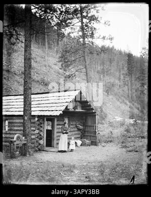 Fotografia di Lee Moorhouse che mostra una capanna di legno, con una donna e un bambino nella zona circostante di Huron, Oregon. Questa immagine fa parte della raccolta PH036. Foto Stock