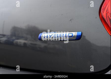 Un'auto ha un emblema blu e argento con la scritta "ibrido". L'auto è parcheggiata in un parcheggio Foto Stock