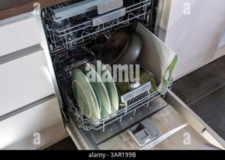 Lavare i piatti in una lavastoviglie completa in una cucina, in Inghilterra. Concetto: Bollette energetiche, consumo domestico di elettricità, efficienza energetica, lavori domestici Foto Stock