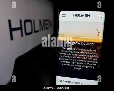 In questa immagine, una persona ha in mano uno smartphone con il sito Web dell'azienda forestale svedese Holmen AB sullo schermo davanti al logo. Foto Stock