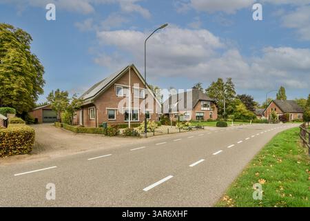 una strada con case sullo sfondo e alberi su entrambi i lati, lungo una strada vuota che conduce ad un parcheggio Foto Stock