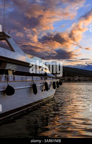 Uno yacht di lusso attraccato vicino all'isola greca di Poros durante un colorato tramonto, con spettacolari nuvole e riflessi dorati sull'acqua. Tramonto sopra t Foto Stock