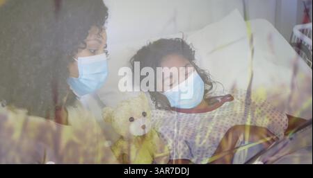 Immagine di erba sopra madre birazziale con maschere facciali e sua figlia sdraiata in ospedale Foto Stock