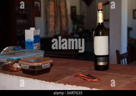 Una bottiglia di vino con etichetta vuota si trova su un bancone in cucina rustico accanto agli avanzi e alla medaglia Foto Stock