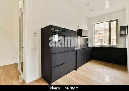 Eleganti mobili neri e elementi di design minimalisti definiscono questo moderno spazio cucina, caratterizzato da grandi finestre che consentono alla luce naturale di riempire la sala. Foto Stock