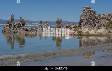 Distinte strutture rocciose sorgono dalle acque poco profonde del Lago Mono, rispecchiando il paesaggio nella superficie ferma. Le montagne circostanti completano la S Foto Stock