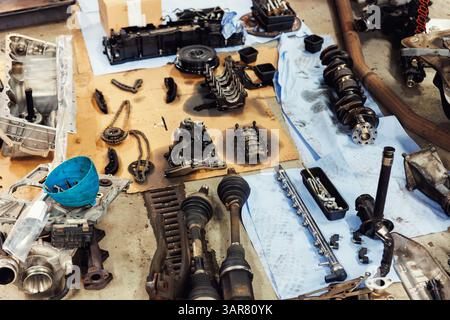 Componenti del motore smontati sparsi sul pavimento dell'officina che mostrano l'albero motore, l'albero di trasmissione, le catene, l'alloggiamento e gli attrezzi. Controllo e riparazione del veicolo Foto Stock