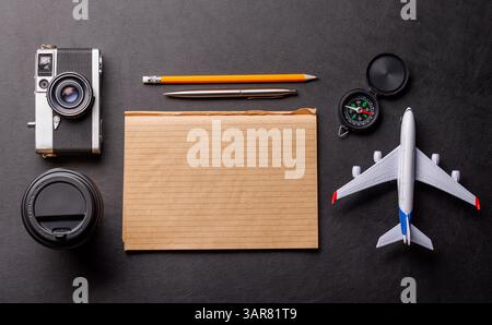 Un piano creativo di una scrivania a tema di viaggio con blocco note per i piani, giocattoli da viaggio come l'aereo e accessori come la fotocamera e la bussola Foto Stock