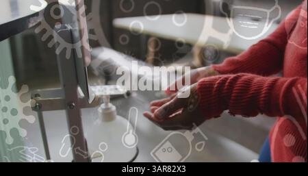 Immagine di cellule e icone del covid 19 sulla donna birazziale che sanifica le mani Foto Stock