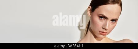 La luce soffusa esalta la bellezza di una giovane donna che si posa con sicurezza su uno sfondo semplice. Foto Stock