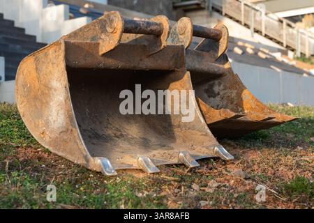 Attacchi per scavo ruggine a terra in un cantiere domestico. Miniescavatore e terreno in lavorazione con terreno rosso fresco e calcestruzzo a gradini Foto Stock