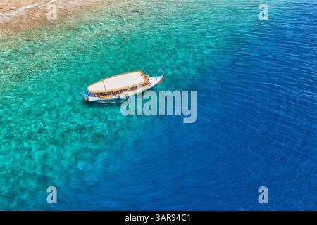Vista aerea della laguna delle Maldive, barca in legno che galleggia su acque turchesi cristalline, perfetta per lo snorkeling, le immersioni e le attività estive all'aperto Foto Stock