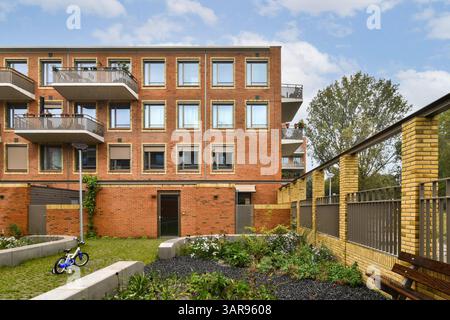 Una struttura residenziale contemporanea caratterizzata da un'attraente facciata in mattoni, balconi e un'area giardino ben tenuta, che promuove un piacevole ambiente abitativo. Foto Stock