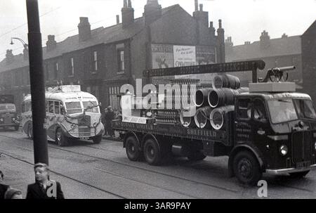 1950, storico carnevale di strada, a Stones of Sheffield, camion aperto sul retro con pile di bottiglie di birra e botti di birra, viaggiando lungo Staniforth Road, Sheffield, Inghilterra, Regno Unito. Sulla parete laterale di una casa a schiera, un poster che promuove la bevanda al malto Ovaltine, lo strapline... Per la salute, per il sonno." Foto Stock