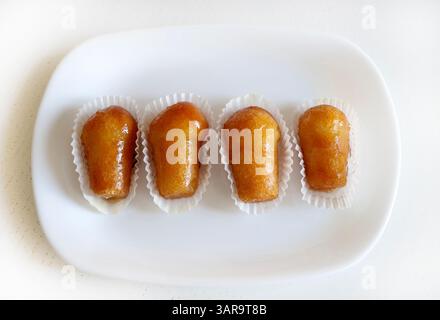 Delizioso rum babà, dolce dessert con alcol fatto lievito imbevuto di rum in un piatto bianco. Sfondo bianco in legno, direttamente sopra, spazio copia. Foto Stock