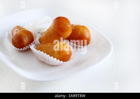 Delizioso rum babà, dolce dessert con alcol fatto lievito imbevuto di rum in un piatto bianco. Sfondo bianco in legno, direttamente sopra, spazio copia. Foto Stock