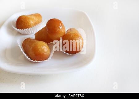 Delizioso rum babà, dolce dessert con alcol fatto lievito imbevuto di rum in un piatto bianco. Sfondo bianco in legno, direttamente sopra, spazio copia. Foto Stock