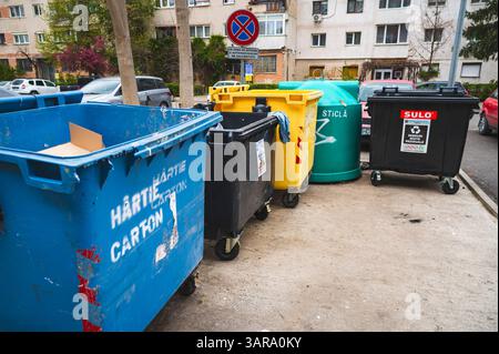 Deva, Romania - 11 aprile 2025 spazio destinato al riciclaggio di contenitori per rifiuti domestici, codici colore, vetro, carta, rifiuti organici Foto Stock