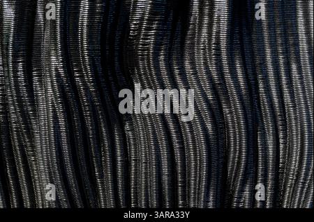 Vista ravvicinata della trama ondulata della fibra di carbonio nera lucida, creando uno sfondo elegante e futuristico Foto Stock