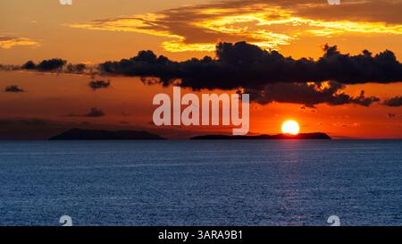 Uno splendido tramonto sull'oceano, con il sole parzialmente nascosto dietro l'orizzonte. Il cielo è pieno di vivaci tonalità arancio e giallo, a contrasto Foto Stock