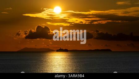 Un tranquillo tramonto sull'oceano, con una grande nave che si staglia contro l'orizzonte luminoso. Il cielo è pieno di nuvole illuminate dal caldo golde Foto Stock