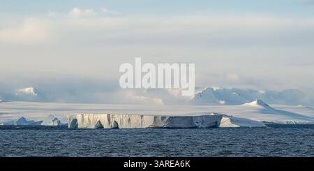 Un grande iceberg tabulare di fronte a montagne innevate vicino a Capo Legoupil, Antartide. Foto Stock