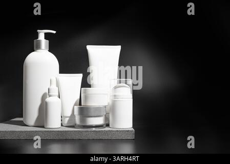 Contenitori di prodotti cosmetici su podio in pietra e sfondo nero, spazio di copia. Vasetto per crema idratante facciale bianco, detergente o tubo di gel per shampoo, Foto Stock
