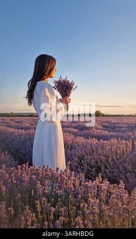 Giovane donna che indossa un abito bianco su un campo di lavanda profumato bouquet di fiori di lavandula viola. Bella sposa in armonia con la natura, matrimonio happ Foto Stock