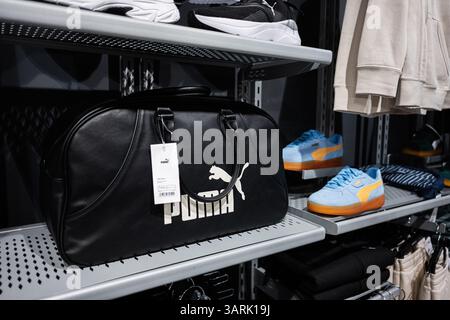 Khmelnytskyi, Ucraina - 16 aprile 2025: Una borsa nera Puma da palestra e scarpe da ginnastica vivaci esposte sugli scaffali all'interno di un ambiente di vendita al dettaglio. Foto Stock