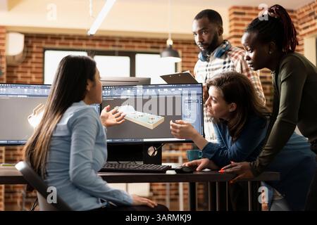 Professionisti creativi maschili e femminili che elaborano idee per migliorare una scena 3D al computer. Artisti digitali multietnici collaborano per ottimizzare i dettagli delle mesh utilizzando software CAD specializzati. Foto Stock