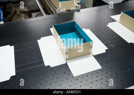 Produzione di imballaggi decorativi in una fabbrica con particolare attenzione alle scatole di cartone colorate che si spostano lungo il nastro trasportatore Foto Stock