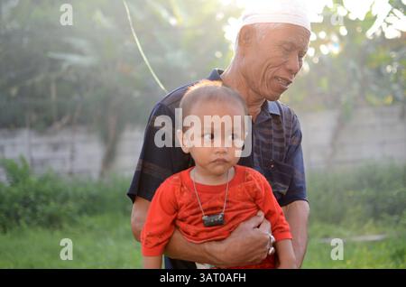 09 luglio 2013 - Sidoarjo, Giava orientale, Indonesia - Un nonno che tiene suo nipote nel campo profughi sciita di Sidoarjo. Un totale di 93 bambini, di età compresa tra i 6 e i 18 anni, sono fuggiti dalla violenza sciita. Il governo provinciale di Giava orientale vieta ai bambini rifugiati sciiti di frequentare la scuola fuori dai campi. Questo Ramadan segna un anno dall'espulsione della comunità sciita a Sampang. Hanno spostato due campi profughi, ma fino a questo momento non ci sono segni di sciiti - Sampang ha permesso di tornare a casa. (Immagine di credito: © Arief Priyono/ZUMAPRESS.com) Foto Stock